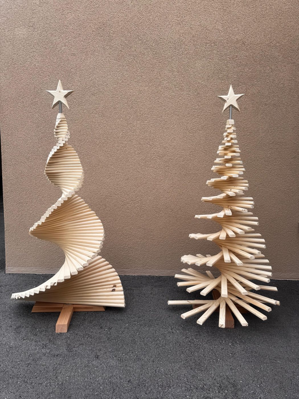 Deux sapins de Noël en bois clair surmontés d'une étoile, l'un en spirale, l'un en lattes étagées